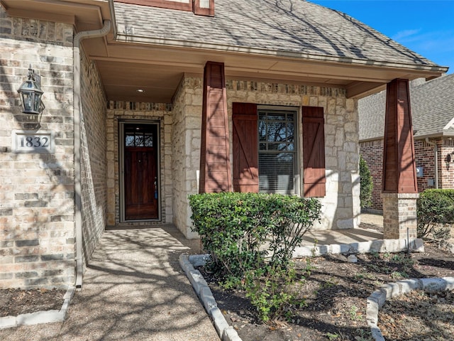 doorway to property with a porch, stone siding, and roof with shingles