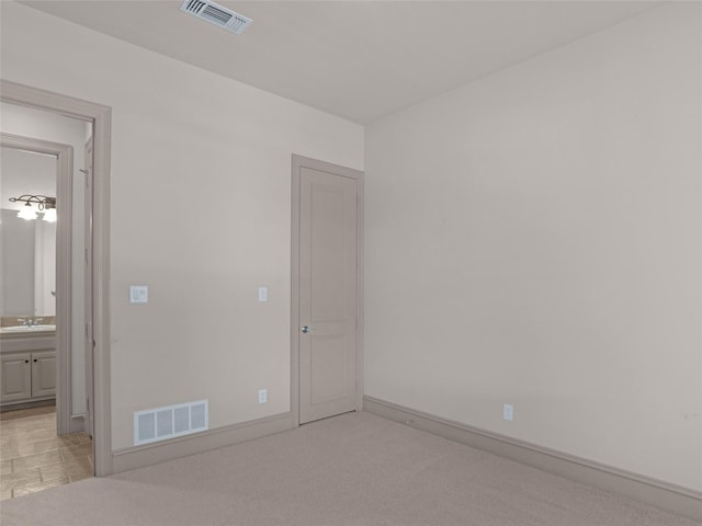 unfurnished bedroom featuring baseboards, light colored carpet, visible vents, and a sink