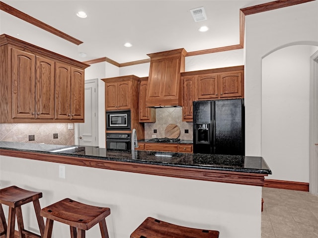 kitchen featuring visible vents, premium range hood, a breakfast bar, arched walkways, and black appliances