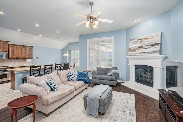 living room with ceiling fan, vaulted ceiling, recessed lighting, a fireplace, and wood finished floors