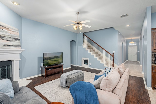 living area featuring stairway, wood finished floors, visible vents, arched walkways, and a glass covered fireplace