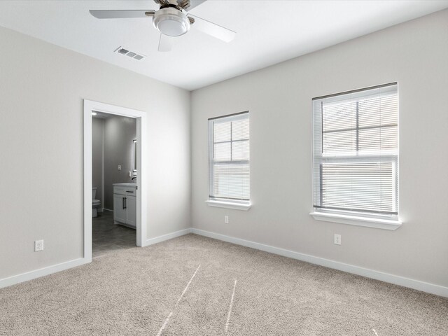 unfurnished bedroom with carpet flooring, ensuite bathroom, visible vents, baseboards, and a ceiling fan