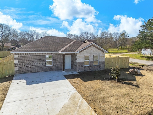 single story home featuring fence, a shingled roof, concrete driveway, stone siding, and brick siding