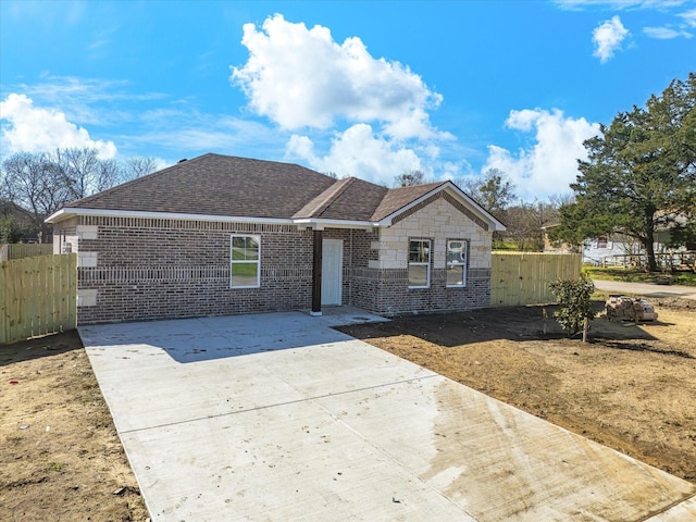view of front facade with driveway, a shingled roof, fence, a patio, and brick siding
