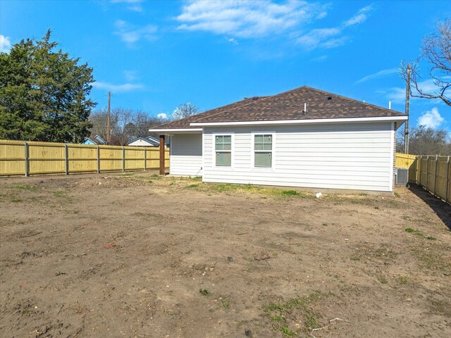 rear view of house featuring roof with shingles, central AC, and a fenced backyard