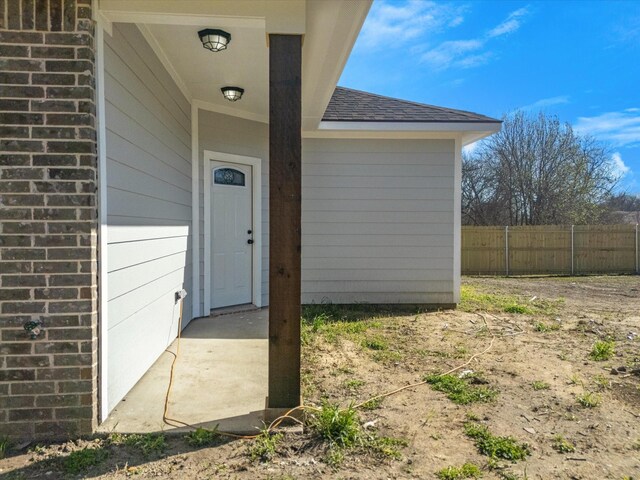 doorway to property with fence and a shingled roof