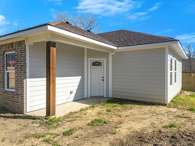 exterior space featuring brick siding and roof with shingles
