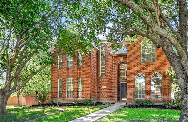 view of front of property with brick siding, a front yard, and fence