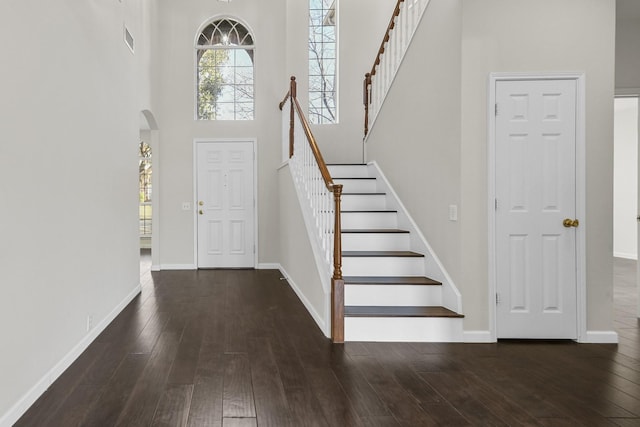 entryway with arched walkways, visible vents, a towering ceiling, and wood-type flooring