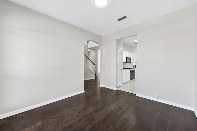 unfurnished living room with visible vents, wood finished floors, stairway, arched walkways, and baseboards