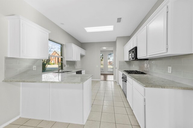 kitchen with light stone counters, light tile patterned floors, a peninsula, black appliances, and a sink