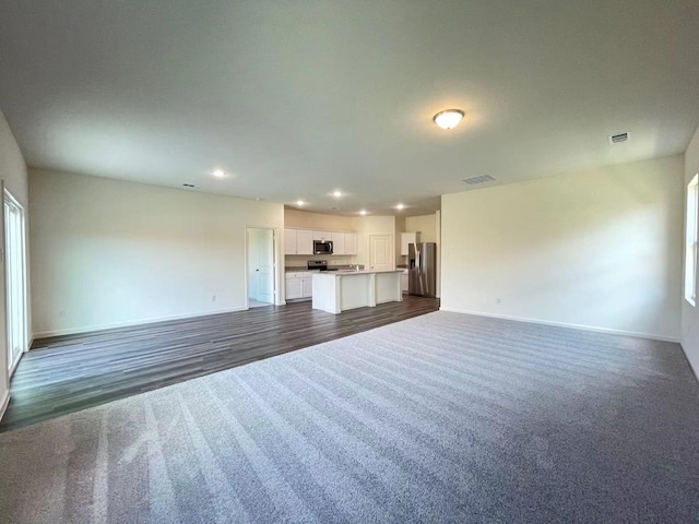 unfurnished living room featuring dark wood finished floors, recessed lighting, baseboards, and dark carpet