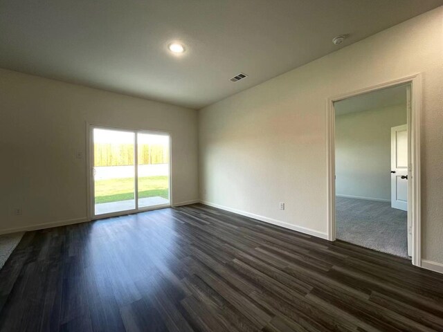 empty room featuring dark wood-style floors, visible vents, and baseboards