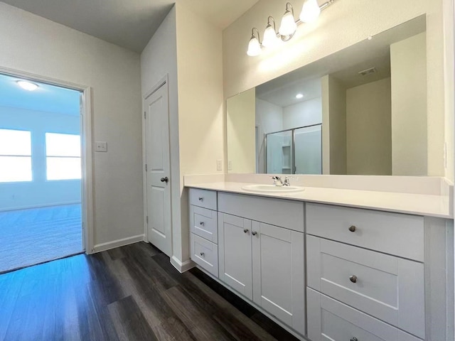 bathroom featuring vanity, wood finished floors, baseboards, and a shower with door