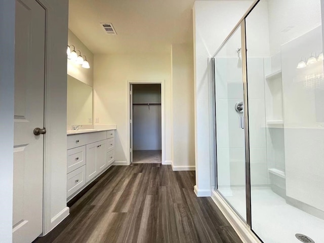 bathroom featuring vanity, wood finished floors, visible vents, a shower stall, and a walk in closet