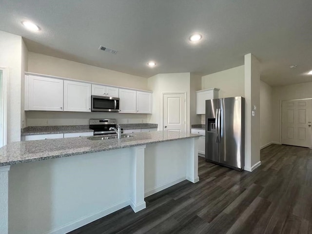 kitchen featuring a center island with sink, visible vents, a sink, stainless steel appliances, and white cabinetry