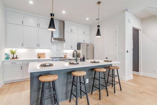 kitchen featuring decorative backsplash, freestanding refrigerator, light wood-style floors, wall chimney exhaust hood, and a sink