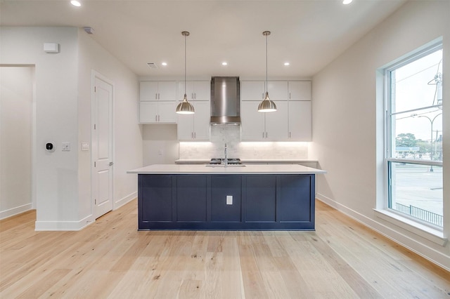 kitchen with light wood-style floors, backsplash, wall chimney exhaust hood, and white cabinets