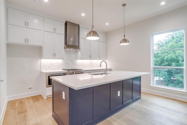 kitchen featuring backsplash, wall oven, white cabinets, wall chimney exhaust hood, and a sink