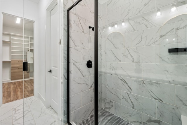 bathroom featuring a spacious closet, marble finish floor, and a stall shower