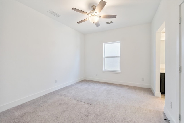 spare room with light carpet, visible vents, baseboards, and ceiling fan