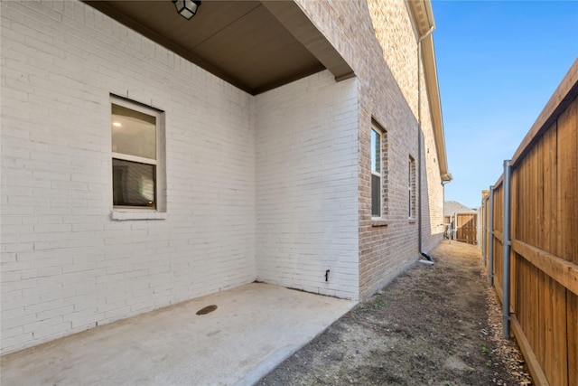 view of side of property featuring fence, a patio area, and brick siding