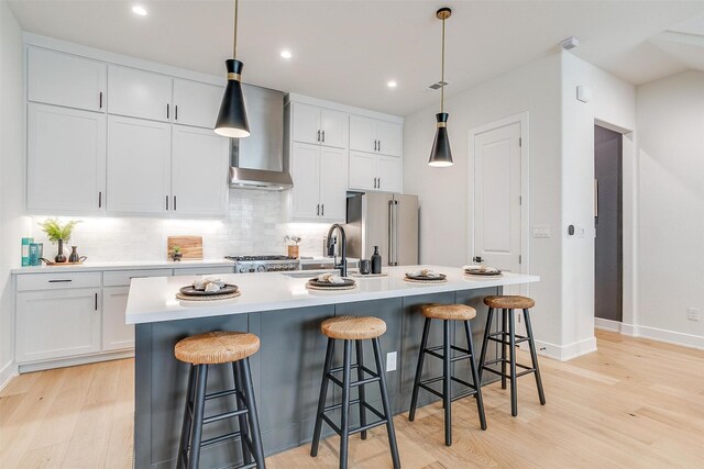 kitchen featuring freestanding refrigerator, a sink, decorative backsplash, light wood-style floors, and wall chimney range hood