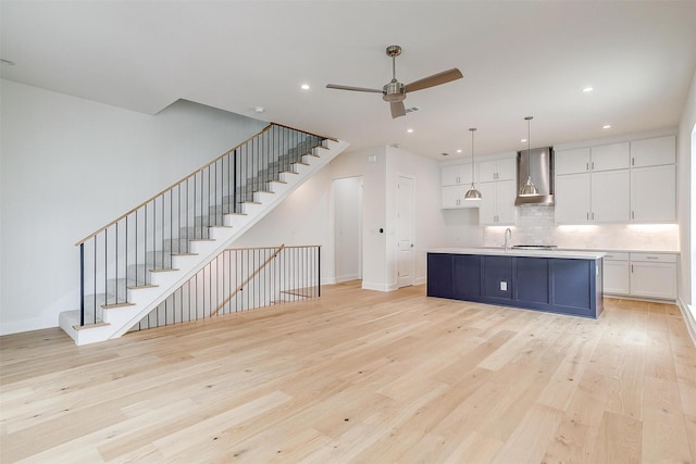 kitchen featuring light wood-type flooring, white cabinetry, tasteful backsplash, and wall chimney range hood