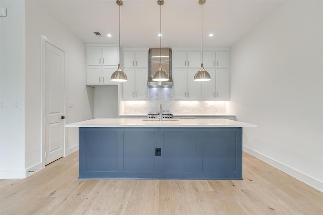 kitchen featuring light wood finished floors, backsplash, an island with sink, light countertops, and white cabinets