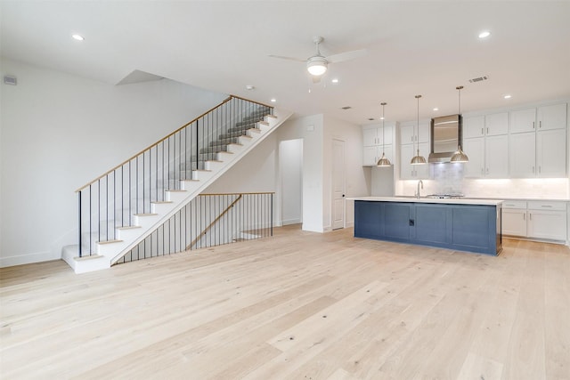 kitchen featuring light wood finished floors, hanging light fixtures, light countertops, white cabinets, and wall chimney exhaust hood