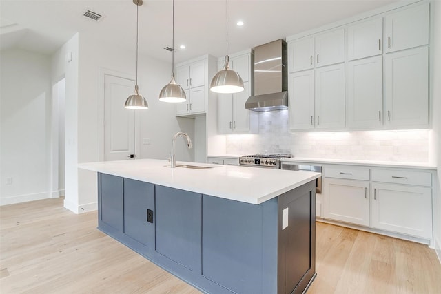 kitchen featuring a sink, light wood-style floors, gas range, wall chimney exhaust hood, and backsplash