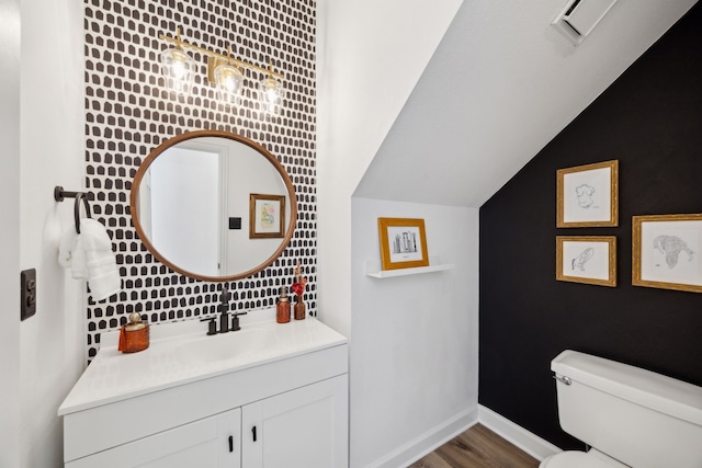 half bathroom with vanity, wood finished floors, baseboards, vaulted ceiling, and toilet