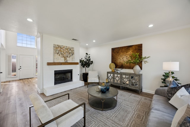 living room with wood finished floors, recessed lighting, a fireplace, crown molding, and baseboards