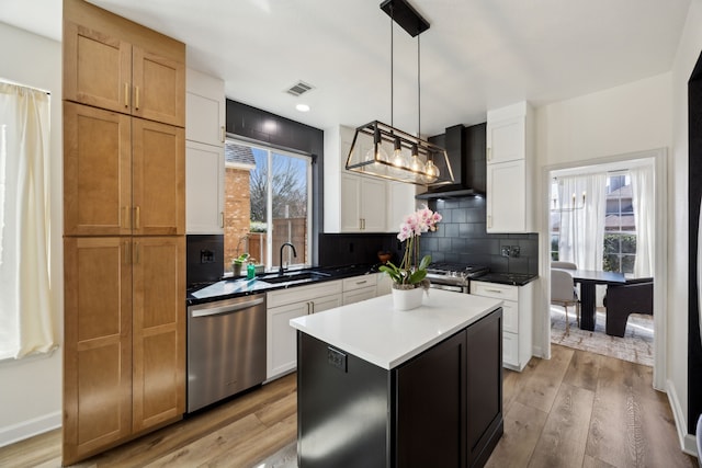 kitchen featuring visible vents, a sink, stainless steel appliances, wall chimney exhaust hood, and backsplash