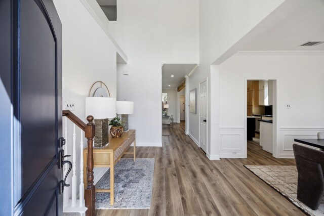 foyer with visible vents, a wainscoted wall, ornamental molding, wood finished floors, and stairway