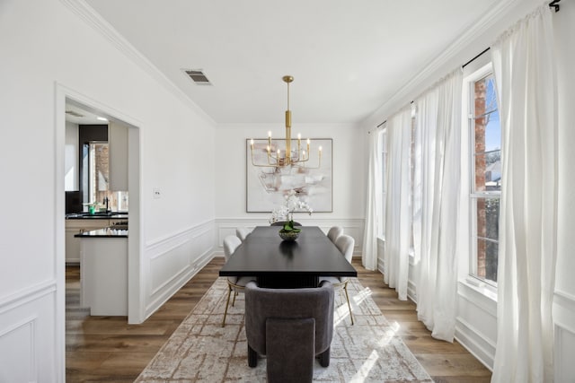 dining room with visible vents, a notable chandelier, wood finished floors, crown molding, and a decorative wall