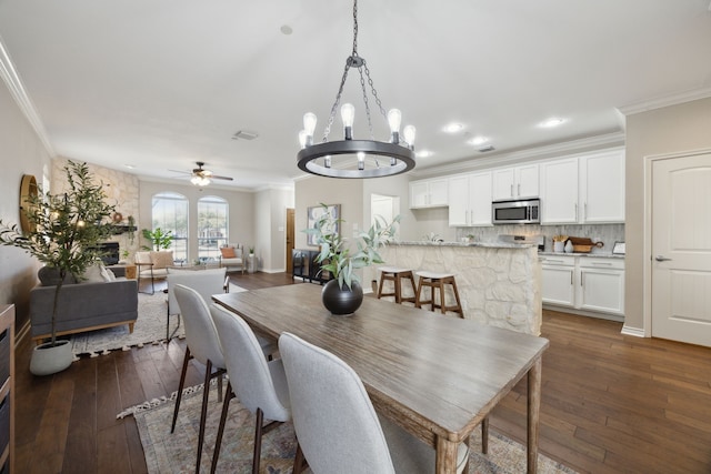 dining room with dark wood-style floors, ornamental molding, and ceiling fan with notable chandelier