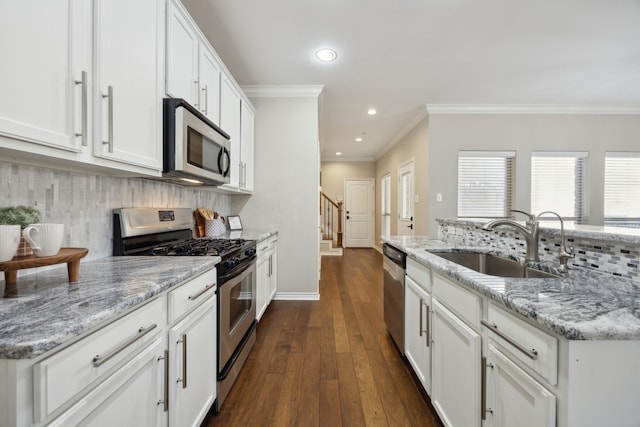 kitchen featuring backsplash, ornamental molding, white cabinets, stainless steel appliances, and a sink