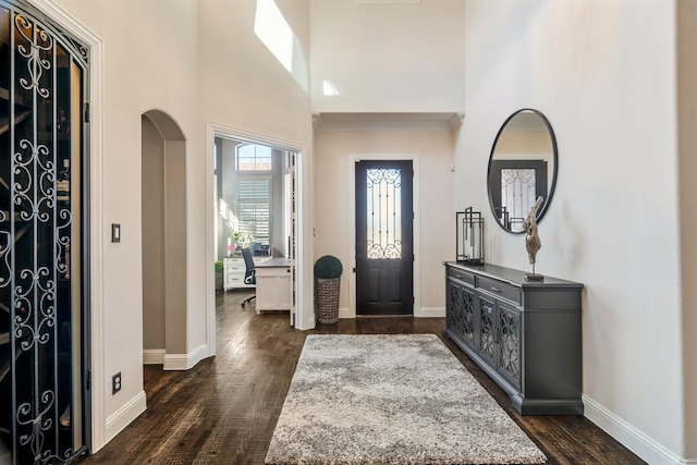 entryway featuring arched walkways, dark wood-type flooring, baseboards, and a towering ceiling