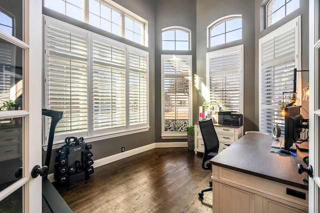 home office with dark wood finished floors, a high ceiling, and baseboards