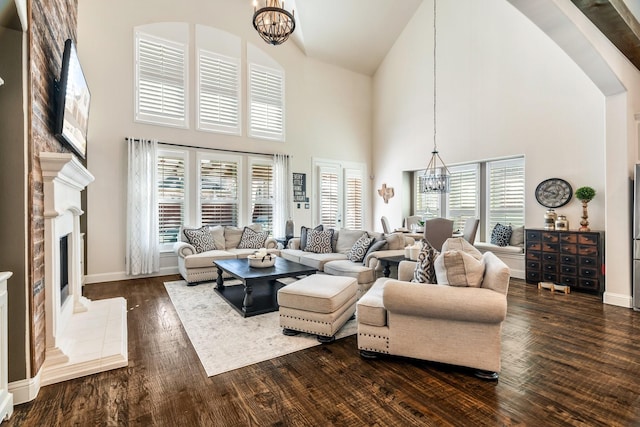 living area featuring high vaulted ceiling, an inviting chandelier, a fireplace with raised hearth, and dark wood finished floors