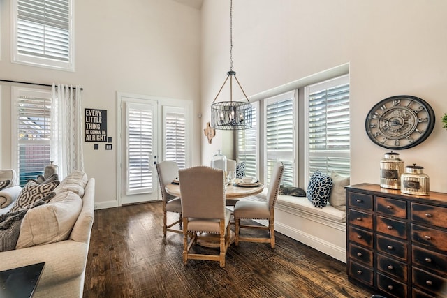 dining area with dark wood-style floors, an inviting chandelier, baseboards, and a towering ceiling