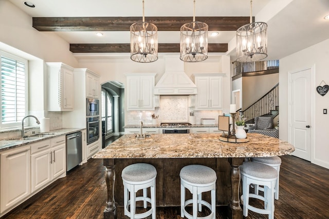 kitchen featuring a kitchen island, custom range hood, a kitchen breakfast bar, appliances with stainless steel finishes, and a sink