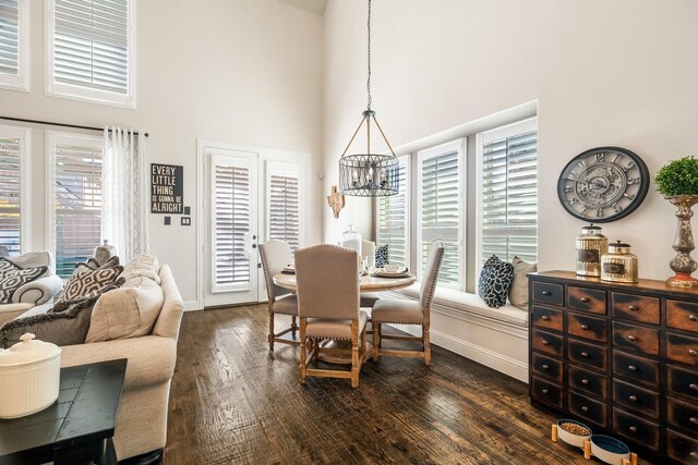 dining area featuring dark wood-type flooring, a healthy amount of sunlight, a towering ceiling, and an inviting chandelier