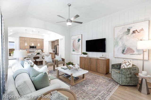 living room featuring light wood-type flooring, arched walkways, a ceiling fan, and vaulted ceiling