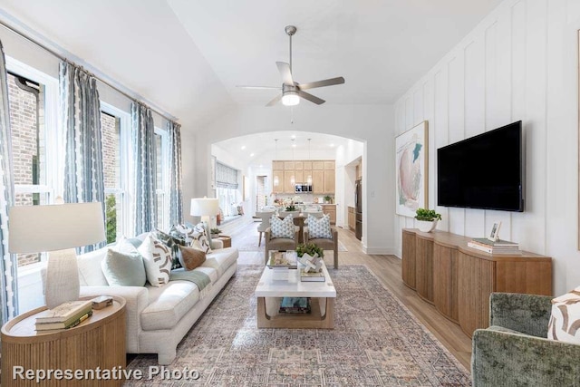 living area with arched walkways, light wood-style floors, lofted ceiling, and a ceiling fan