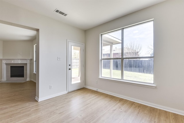 interior space with visible vents, light wood-style flooring, a brick fireplace, and baseboards