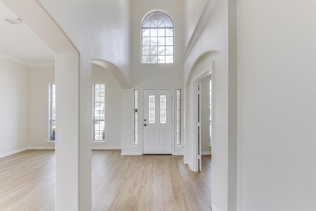 entrance foyer with visible vents, arched walkways, a healthy amount of sunlight, and light wood finished floors