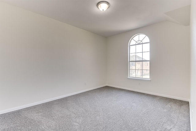 carpeted spare room featuring lofted ceiling and baseboards