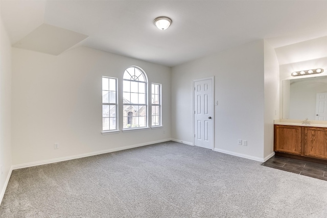 empty room with dark carpet, baseboards, and a sink